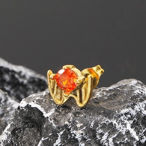 Macro shot of gold bat wing stud earring with orange cubic zirconia on dark stone