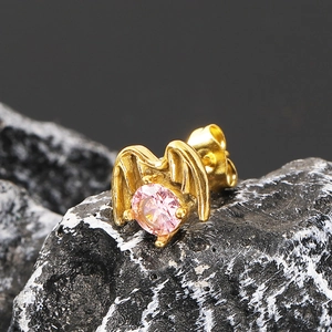 Macro shot of gold punk wing stud earring with a pink zircon stone on volcanic rock