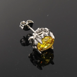 Macro shot of a yellow zircon stud earring with a crown claw setting on black mirror