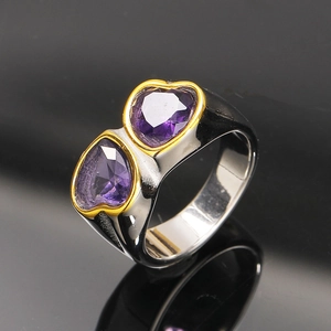 Détail macro de deux cœurs en zircon violet avec bordures dorées sur anneau argenté