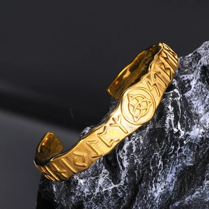 Bracciale vichingo dorato con incisioni runiche e nodo celtico su fondo di pietra
