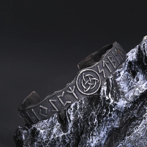 Dettaglio del bracciale vichingo con rune nordiche e nodo Triquetra su roccia nera