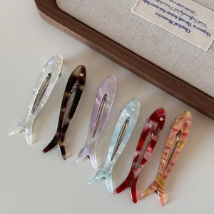 Detailed close-up showing six colorful acetate fish hair clips with brand logo engraving