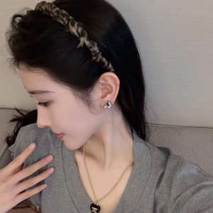 Detail of leopard print headband, silver stud earrings and heart necklace on model