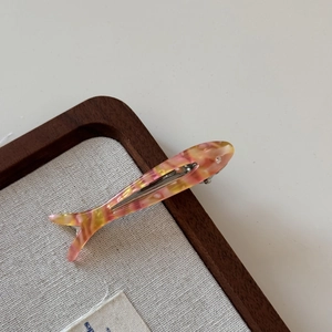 Detailed close-up of fish-shaped acetate hair clip with amber texture and rhinestone eye