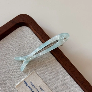 Close-up of light blue fish-shaped acetate hair clip with pearl finish and rhinestone detail