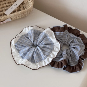 Detail view of two large ruffled hair scrunchies with blue patterns and contrast edging