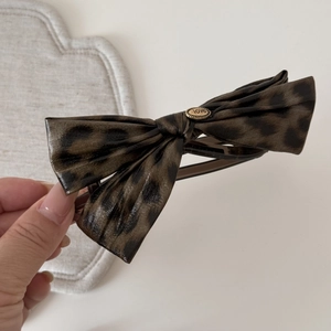 Detail shot of leopard print bow hair clip with gold metal buckle featuring love engraving