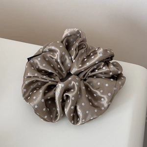 Close-up of champagne satin scrunchie with white polka dots and fashion textile label
