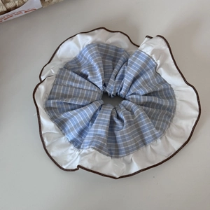 Detailed view of oversized blue plaid scrunchie with white ruffle trim and brown edges