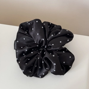 Detailed close-up of a large black satin scrunchie with white polka dots and fashion tag