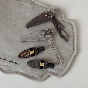 Detailed set of four rhinestone tassel hair clips and pearls on a beige linen tray