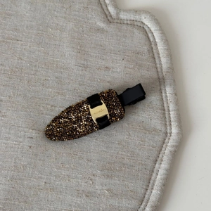 Close-up of duckbill hair clip with dark brown rhinestones and golden smile engraving