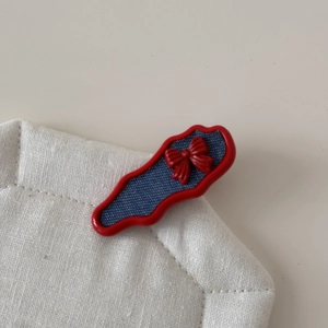 Detail view of wavy red hair clip with blue denim patch and central 3D bow accent