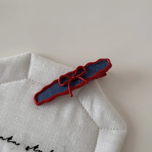 Red wavy edge hair clip with blue denim pattern and bow detail on a fabric background