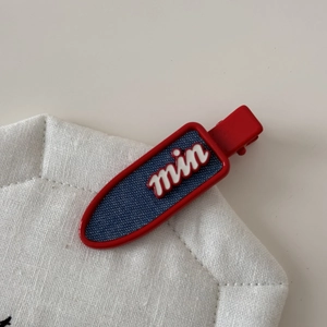 Detailed close-up of red hair clip with blue denim inlay and white 'min' lettering