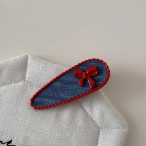 Blue denim hair clip with red scalloped trim and a bow on white linen background