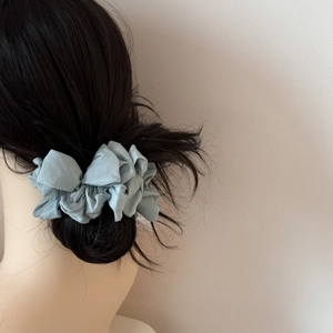 Chouchou plissé bleu clair en tissu doux porté sur un chignon de cheveux bruns