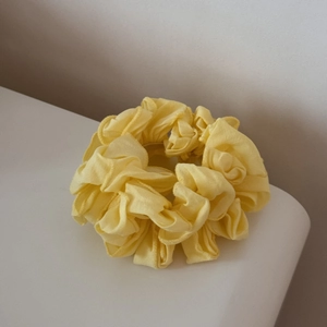 Détail d'un chouchou jaune vif plissé en tissu léger pour une coiffure de queue de cheval