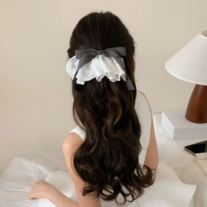 Preppy plaid bow hair clip with white lace trim shown on a model in a cozy indoor setting