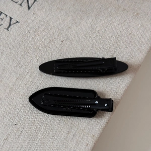 Close-up of black glossy metal hair clips in oval and shield shapes on linen texture