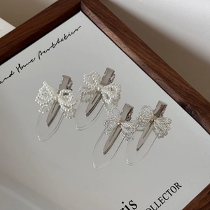 Close-up of four handmade pearl bow hair clips and acrylic bead pins on a mirror tray