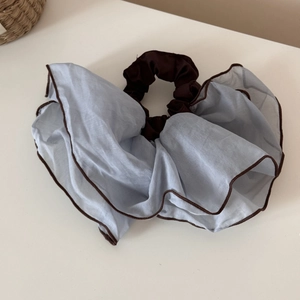 Detailed view of grey-blue mesh scrunchie with brown trim and pleated floral design