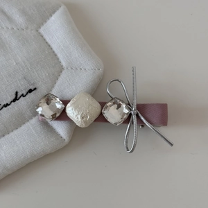 Détail d'une barrette rose avec strass, perle carrée et nœud en fil argenté brillant
