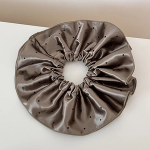 Detailed view of taupe satin scrunchie featuring black polka dots and metallic sheen