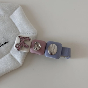 Détail d'une pince à cheveux rose avec nœud, strass et perles sur un support blanc