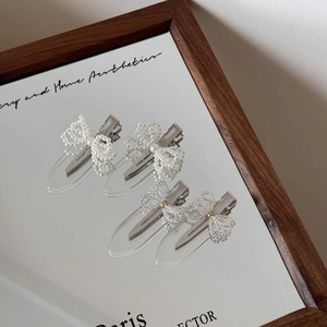 Detailed view of pearl and transparent bead bow hair clips on a mirror surface
