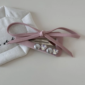 Détail d'une pince à cheveux avec nœud en tissu rose, perles et cristaux en cœur