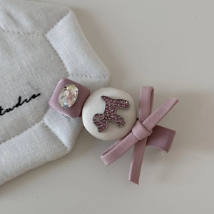 Détail de pince à cheveux avec nœud en satin rose, chien en strass et bouton en tissu