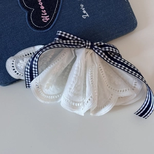Close-up of layers of white embroidery lace with a navy plaid bow hairclip detail