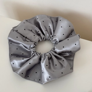 Macro detail of glossy silver satin scrunchie with classic black polka dot pattern
