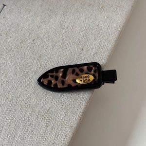 Close-up of tortoise shell fabric hair clip with a gold handmade logo on beige linen