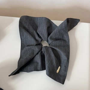 Détail d'une pince à cheveux en tissu rayé gris avec logo en métal doré