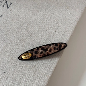 Detail of handmade leopard print hair clip with golden metal label on linen fabric