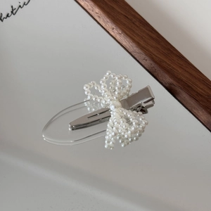 Elegant pearl bow hair clip with silver duckbill base displayed on a reflective mirror