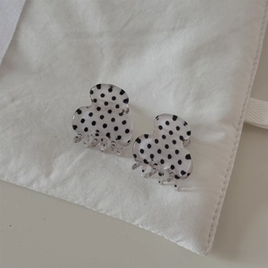 Close-up of mini white hair claws with black polka dots on a textured fabric