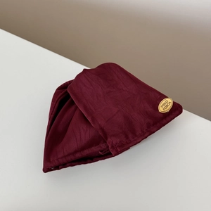 Primer plano de textura de satén burdeos con etiqueta metálica ovalada dorada de marca