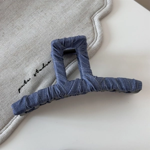 Detail of blue denim fabric texture and raw edges on a large rectangular hair claw clip