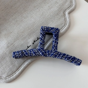 Close-up of blue and white checkered striped denim fabric hair claw clip on beige linen