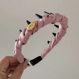 Detalle de diadema de satén rosa con tachuelas negras y placa metálica dorada