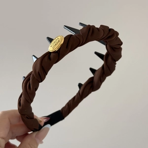 Detalle de diadema de satén marrón oscuro plisada con tachuelas negras y etiqueta de metal