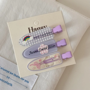 Détail de trois barrettes violettes avec motifs floraux et arc-en-ciel sur carte blanche
