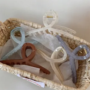 Set di grandi pinze per capelli traslucide in colori neutri in un cesto di paglia