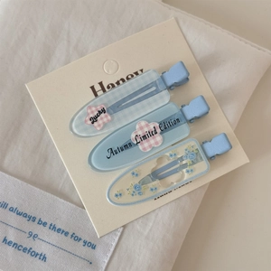 Détail de trois barrettes à cheveux bleues en acrylique avec motifs floraux sur carte
