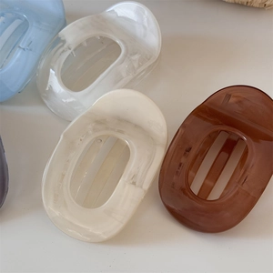 Detail of four colorful acetate hair claws in blue, white, beige, and amber colors