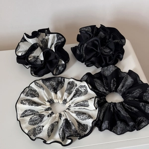 Detailed close-up of four pleated scrunchies featuring black and white abstract patterns